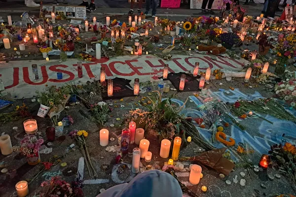 A photo of a vigil in the aftermath of the shooting of Corey Ruiz shows a number of lit candles arrancged on the ground, alongside flowers, chalk drawings, and protest signs.